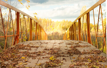 Yellow village bridge.Fallen leaves on a wooden bridge.Autumn forest in the distance and dark beautiful clouds in the autumn sky