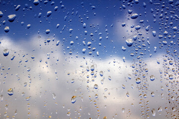 Rain drops on a window. Natural abstract pattern. Blue sky background. Selective focus. 
