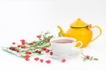 Obraz na płótnie Canvas Cup of rose hip herbal tea with rose-hip fruits and pot on white background. Dog rose autumn or winter healthy tea. Strengthening the immune system