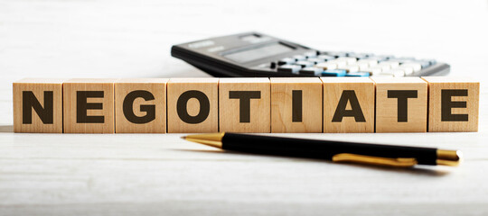 The word NEGOTIATE is written on wooden cubes between a calculator and a pen. Business concept.