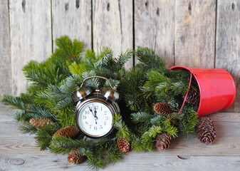 Christmas clock on Christmas Eve. An old alarm clock surrounded by fir branches spilling out of a...