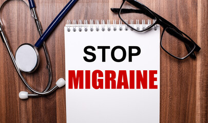 STOP MIGRAINE is written on white paper on a wooden background near a stethoscope and black-framed glasses. Medical concept