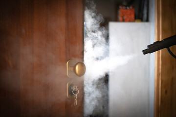 Obraz na płótnie Canvas disinfection and sanitization with steam at home, steam flow is directed to the door handle and keys in the lock