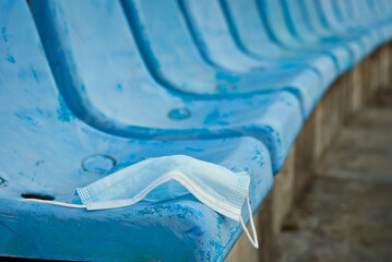 Obraz premium Blue protective mask on the background of chairs. The mask was left by the fan at the stadium. The concept of prohibition during a coronavirus pandemic.