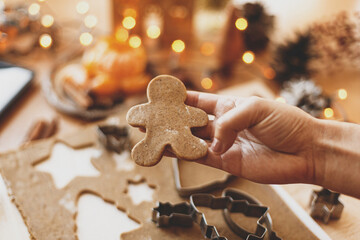 Person holding gingerbread man cookie on background of festive lights. Christmas tradition