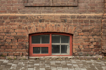 Red window of the basement floor in an old brick building, in front of the building there is a...