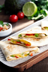 Still life on a table with four chicken and cheese quesadillas. In the background pico de gallo and lime