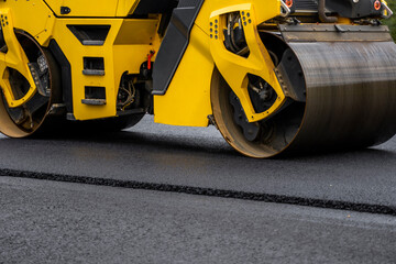 Asphalt road roller with heavy vibration roller compactor press new hot asphalt on the roadway on a road construction site. Heavy Vibration roller at asphalt pavement working. Repairing.