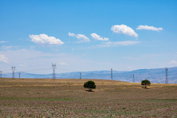 Electricity lines on the agricultural fields in steppe with cloudy sky. High voltage electricity lines. Industrial background photo. Electricity production.