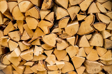 Pile of stacked triangle firewood prepared for fireplace and boiler.dry chopped firewood logs ready for winter.Birch background.