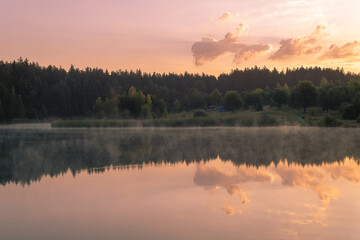 Beautiful pink sunrise over the surface of the lake.. Reflections of clouds on the water.