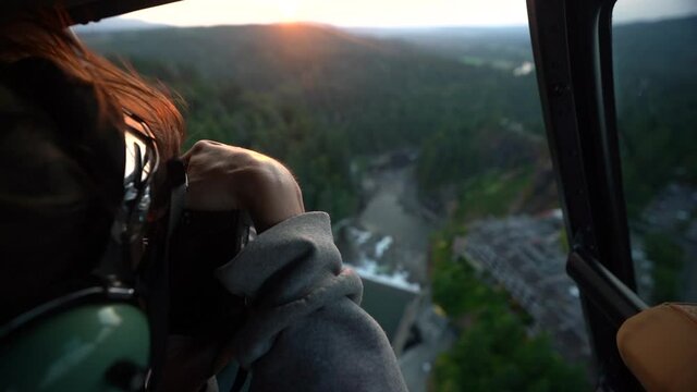 Female Photographer Taking Pictures From Helicopter Cabin During Sunset Flight. Flying Above Snoqualmie Falls, Washington State USA