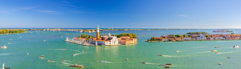 Fototapeta na wymiar Aerial panoramic view of Venetian Lagoon with San Giorgio Maggiore island, Lido island and Giudecca island, sailing boats in Giudecca Canal, blue sky, Venice city, Italy. Panoram of Venetian Lagoon