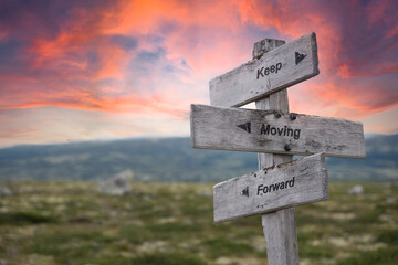 keep moving forward text engraved in wooden signpost outdoors in nature during sunset and pink...