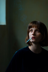 Fototapeta premium Portrait of a young beautiful girl of generation Z smoking a cigarette at the entrance of the house