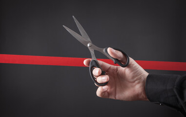 Male hand cutting red ribbon with a scissors.