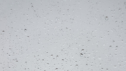 Wet with water drops glass window with light grey rainy background, closeup.