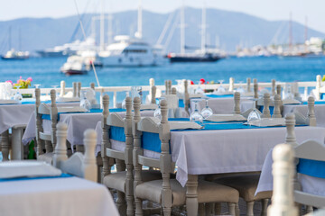 Elegant table setting with fork, knife, wine glass, white plate and blue napkin in restaurant. Turkey. Beach cafe near sea