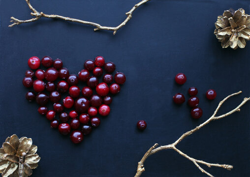 Composition with cranberries in shape of heart, golden twigs and branches on black background. Holiday, winter and December concept. Copy space.