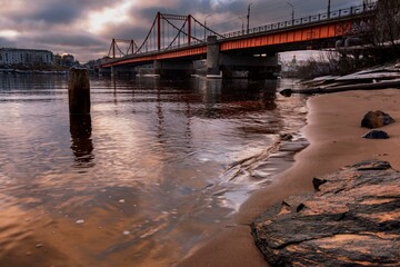 cityscape with a view of the orange bridge over the river against the backdrop of the cloudy sky.