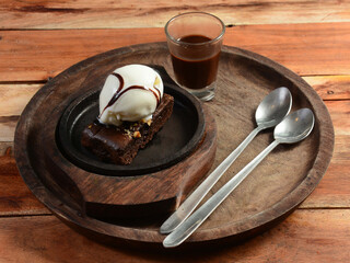 sizzling chocolate brownie is a sweet dish made using scoop of ice-cream on top served with a generous pouring of melted chocolate syrup on wooden plate. server hot. selective focus