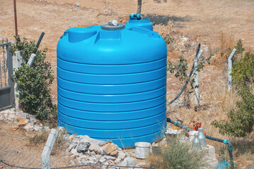 A large blue water tank near a private farm or garden in a dry area. Concept of equipment for...