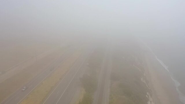 Aerial over a foggy freeway US 101 Pacific Coast Highway with traffic along the coast of California.
