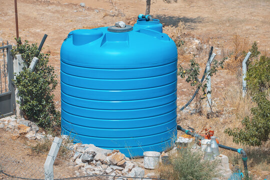 A large blue water tank near a private farm or garden in a dry area. Concept of equipment for agriculture and drought