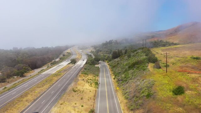 Aerial over a foggy freeway US 101 Pacific Coast Highway with traffic along the coast of California.