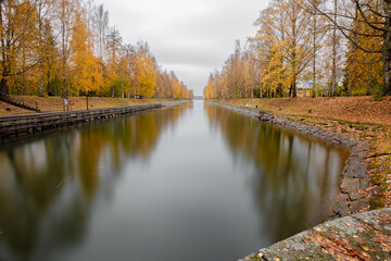 Fototapeta na wymiar View of the Vääksu canal, in autumn, yellow birches on the bank and reflection in the water. It's a nasty day .