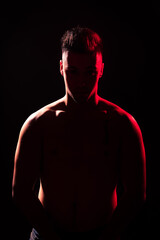 Fototapeta premium Young adult illuminated by red and white lights with a black background.