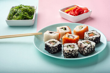 Different rolls on a blue plate with ginger in the background. Rolls with Chuka salad.