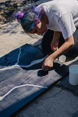 Latin hispanic woman with colorful hair painting a wooden board with black and white paint. Outdoors painting hobbie