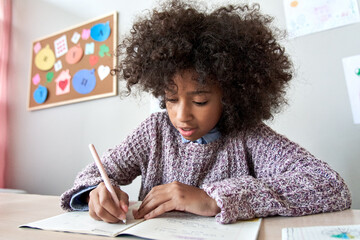 Happy african american black preteen school girl studying in classroom sitting at desk. Smart cute mixed race kid primary school student writing in exercise book doing homework, learning at home. - Powered by Adobe