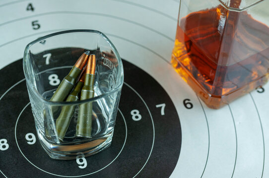 gun casings with a glass of whiskey and a bottle on a wooden table and a target