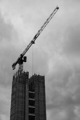 Black and white moody dramatic construction site with crane constructing large tower block