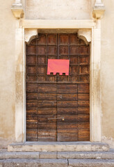 Old wooden portal of an ancient church, with an empty red banner hung on it