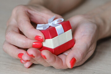 Red gift box of a woman's hands in a beautiful style on a light background. Great design for gift purposes. The concept of the celebration.