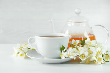 Obraz na płótnie Canvas a cup of tea, a glass kettle and jasmine flowers on the table close-up. background with herbal tea in a cup and kettle and jasmine flowers.