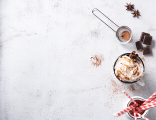 coffee latte with creamy caramel cream, red papper tube and cinnamon in a white mug on a white table