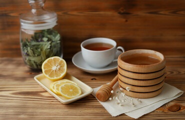A barrel of honey, lemon cut into pieces and herbal tea on a wooden background. Prevention of colds. Selective focus