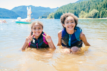 Smiling happy sisters in lifejackets swimming in lake water
