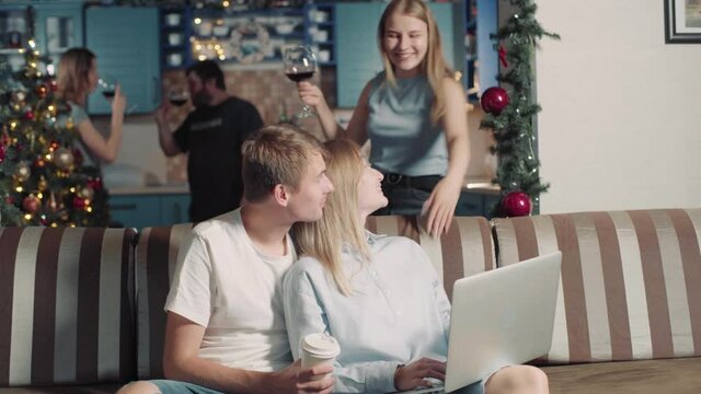 Young Couple Businessmen Working Online While Group Friends Have Fun Celebrate Christmas. Girl And Man Uses Computer. Students Preparing For Exams At University In Dormitory. Friends Call Drink Wine.