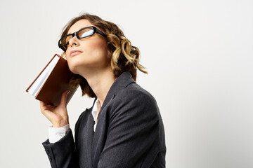 Woman at work with book in hand light background classic suit glasses head