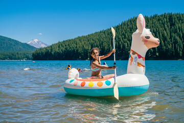 Teen girl paddling on lake in inflatable llama pool floaty