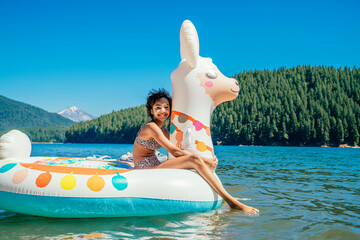 Smiling teen girl sitting on inflatable llama pool floaty in lake in forest in summer