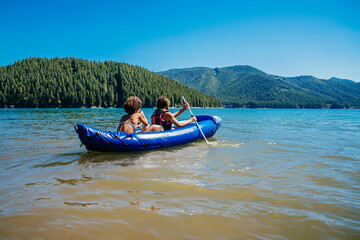Sisters paddling inflatable kayak on lake water in forest