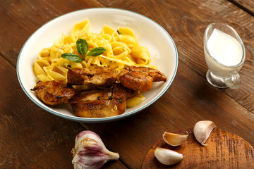 A plate of pasta in a creamy sauce with cheese and chicken on the table next to the garlic board.