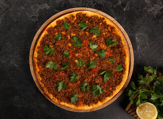 Turkish cuisine. Lahmacun. Turkish round pizza with minced meat, tomatoes, sweet peppers, onions, herbs and lemon on a wooden board on a black table. Background image, copy space, flatlay, top view
