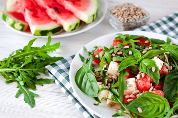 Fresh delicious salad with watermelon, feta cheese, basil leaves, arugula and peeled Sunflower seeds on white plate. Healthy food concept. Close-up.